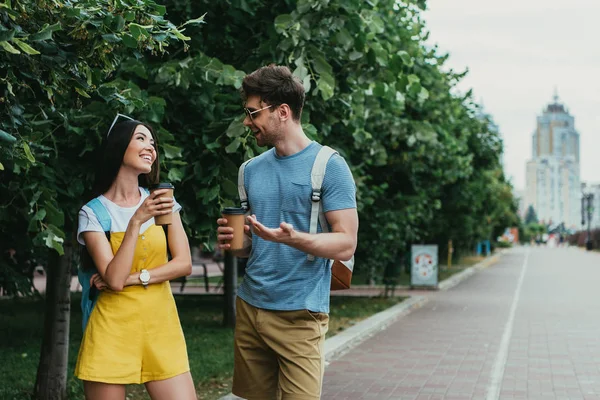 Красивый мужчина и азиатская женщина разговаривают и держат бумажные стаканчики — стоковое фото