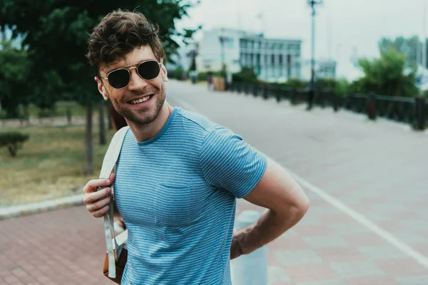 Hombre sonriente y guapo en camiseta con mochila y gafas - foto de stock