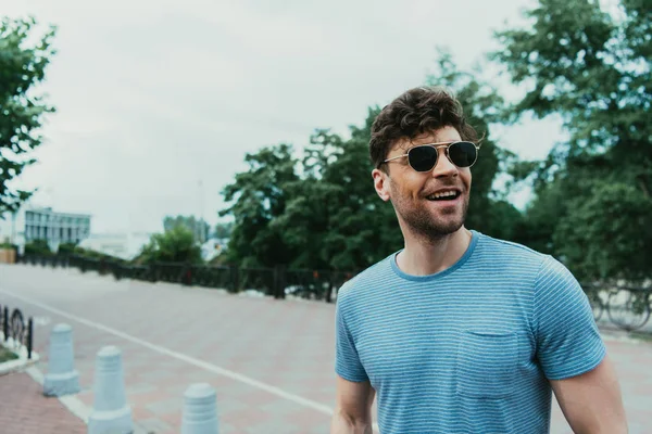 Hombre sonriente y guapo en camiseta y gafas mirando hacia otro lado - foto de stock