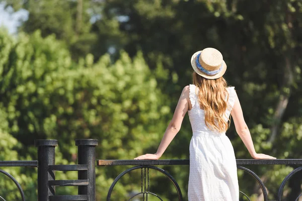 Vista trasera de la chica en vestido blanco y sombrero de paja apoyado en pasamanos - foto de stock