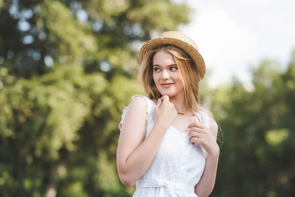 Selective focus of beautiful girl in straw hat and white dress looking away — Stock Photo