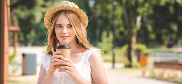 Panoramic shot of beautiful girl in white dress and straw hat holding paper cup and looking away — Stock Photo
