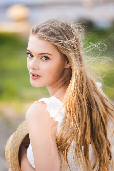 Portraitaufnahme des schönen Mädchens im weißen Kleid mit Strohhut und Blick in die Kamera — Stockfoto