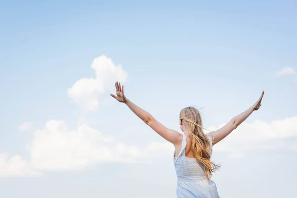 Back view of girl in white dress standing with hands in air — Stock Photo