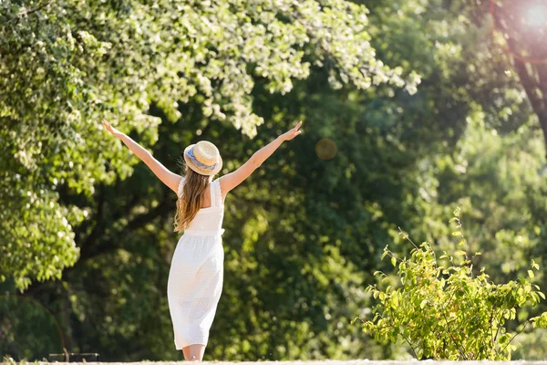 Back view of girl in white dress walking in park with hands in air — Stock Photo