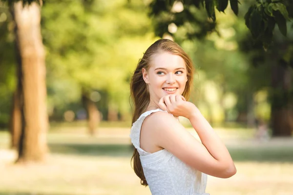 Красива молода дівчина в білій сукні позує, стоячи в парку і дивлячись геть — стокове фото