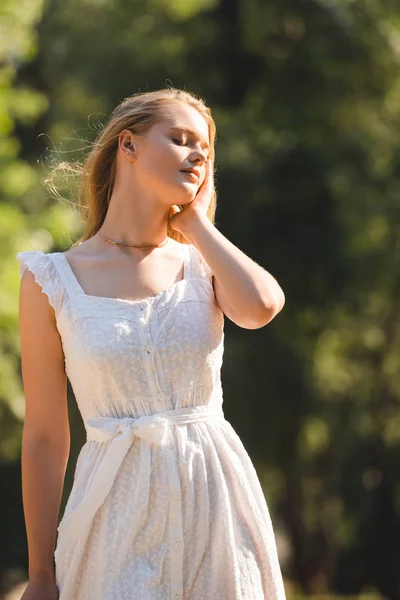 Menina bonita em vestido branco de pé no prado com olhos fechados — Fotografia de Stock