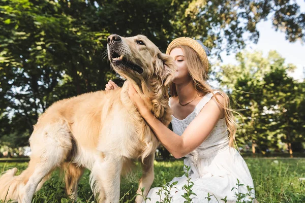 Beautiful girl in white dress and straw hat petting golden retriever — Stock Photo