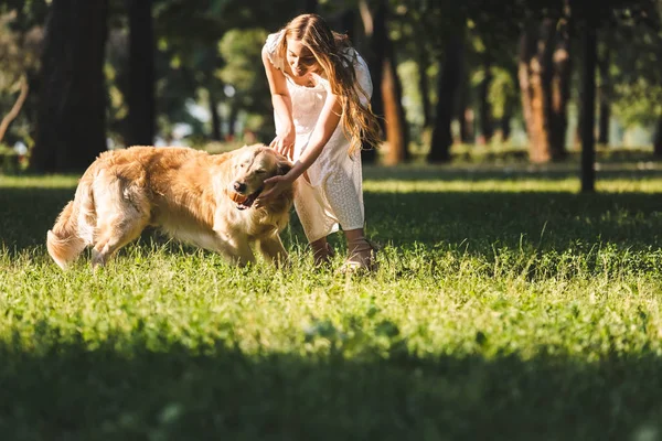 Full length view of beautiful young girl in white dress playing ball with golden retriever on meadow — Stock Photo