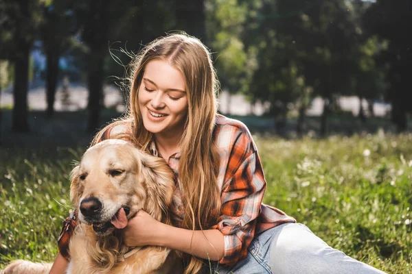Beautiful girl smiling while petting golden retriever and looking at dog — Stock Photo