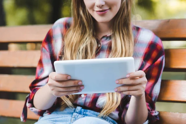 Abgeschnittene Ansicht eines jungen Mädchens in Freizeitkleidung, das auf einer Holzbank im Park sitzt und ein digitales Tablet benutzt — Stockfoto