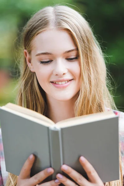 Retrato de la hermosa chica en ropa casual sonriendo mientras lee el libro - foto de stock