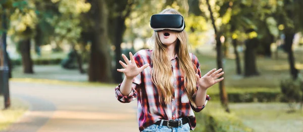 Panoramic shot of surprised young girl in casual clothes using vr headset — Stock Photo