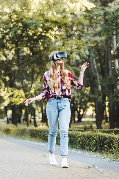 Vue pleine longueur de la jeune fille en vêtements décontractés en utilisant vr casque tout en marchant dans le parc — Photo de stock