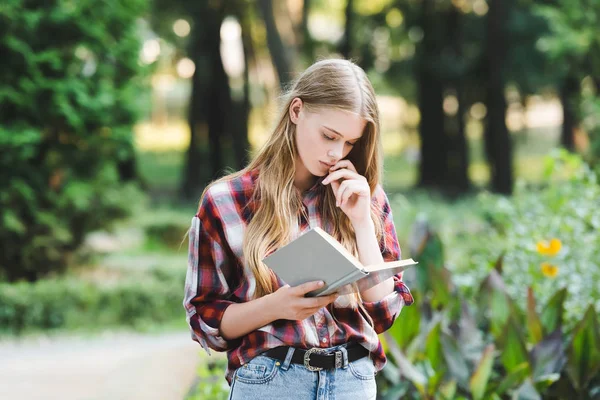 Focused young girl in casual clothes reading book — Stock Photo