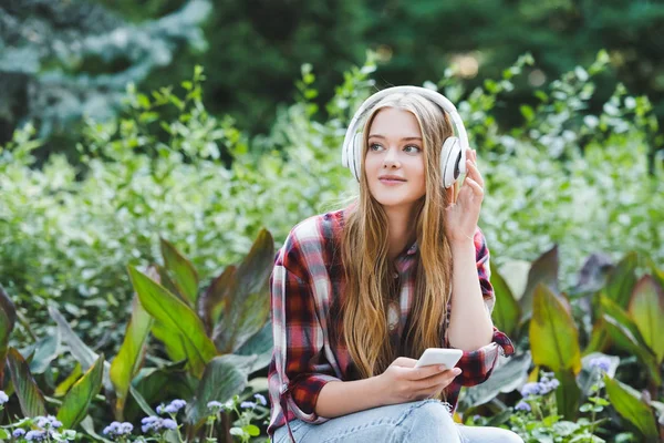 Beautiful girl in casual clothes smiling while listening to musing on headphones and looking away — Stock Photo