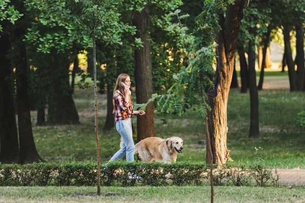 Vista completa de la hermosa chica en ropa casual despertando en el parque con golden retriever y hablando en el teléfono inteligente - foto de stock