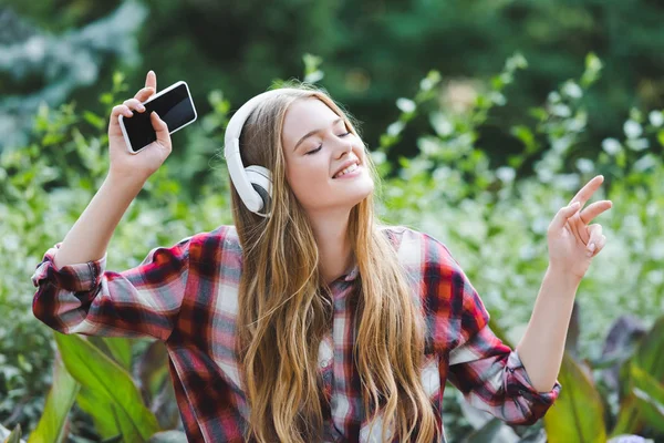 Hermosa chica en ropa casual escuchando musa en los auriculares con los ojos cerrados - foto de stock