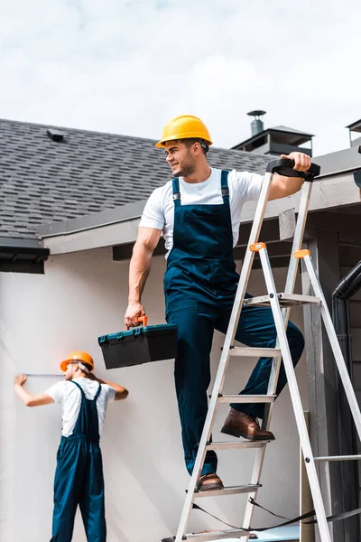 Selective focus of workman standing on ladder with toolbox near coworker — Stock Photo