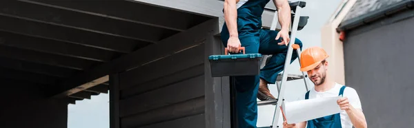 Panoramic shot of builder pointing with finger at paper near happy coworker — Stock Photo