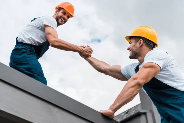 Low angle view of cheerful handymen in helmets holding hands — Stock Photo