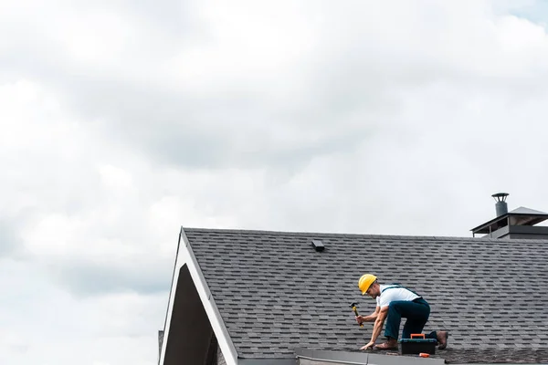 Réparateur dans le casque tenant marteau tout en réparant le toit — Photo de stock