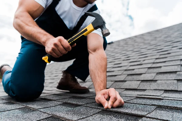 Cropped view of handyman in uniform holding hammer while repairing roof — Stock Photo