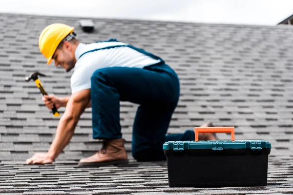 Selektiver Fokus der Werkzeugkiste in der Nähe von Werkstätten, die Hammer auf dem Dach halten — Stockfoto