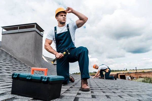 Selektiver Fokus des gut aussehenden Heimwerkers, der Helm berührt, während er Hammer hält — Stockfoto