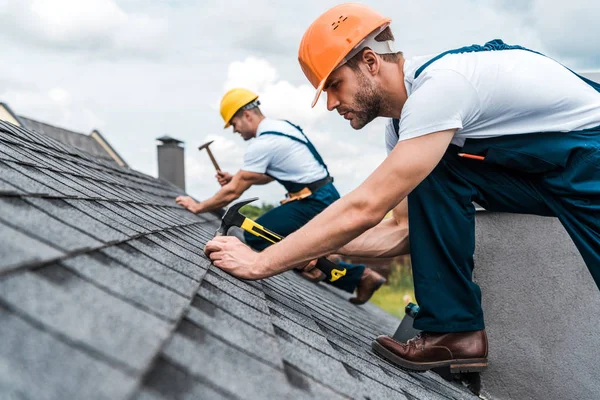 Selective focus of handsome handyman repairing roof with coworker — Stock Photo