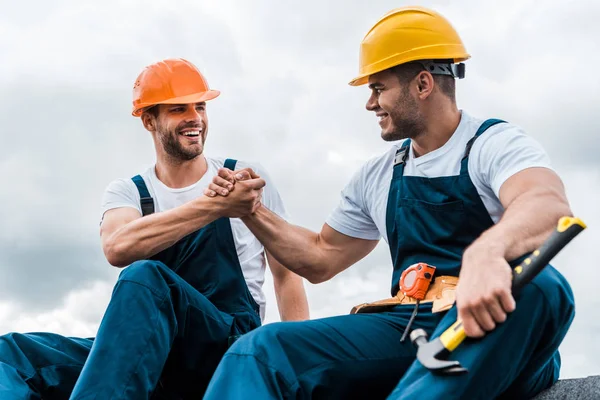 Happy handymen holding hands while smiling against sky — Stock Photo