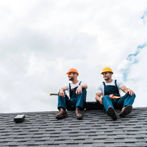 Веселі майстри в касках і уніформі сидять на даху — стокове фото