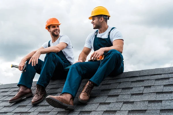 Glückliche Heimwerker in Helmen und Uniform sitzen auf dem Dach — Stockfoto