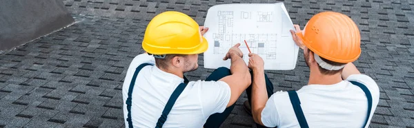 Panoramic shot of builders in helmets looking at blueprint — Stock Photo