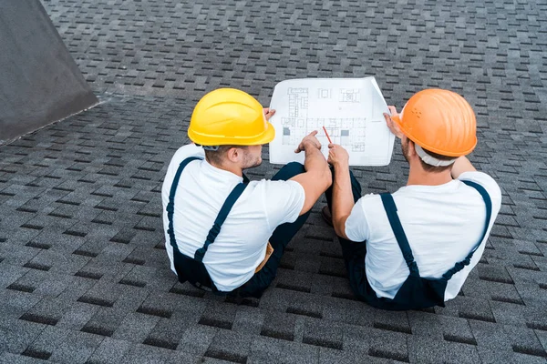 Overhead view of architects in helmets sitting on roof with blueprint — Stock Photo