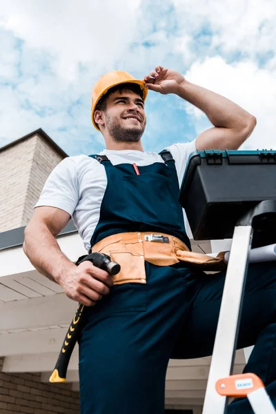 Vue à angle bas du réparateur heureux touchant casque tout en tenant le marteau — Photo de stock