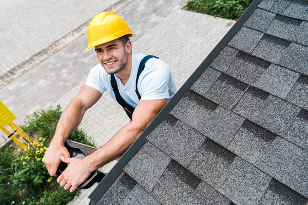 Overhead view of happy man in yellow helmet smiling near roof — Stock Photo