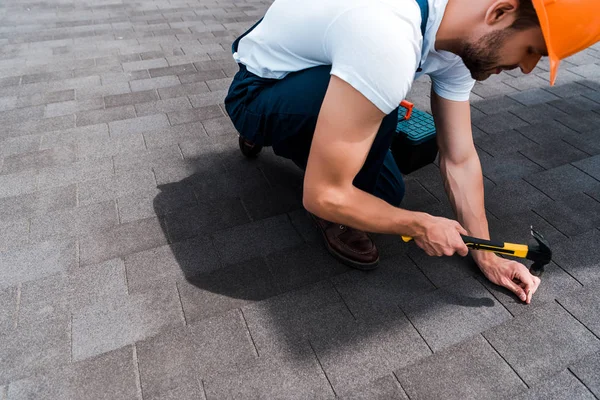 Handyman in uniform holding hammer while repairing roof — Stock Photo