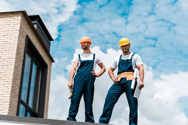 Vista de ángulo bajo de los reparadores guapos de pie con las manos en las caderas - foto de stock