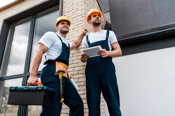 Niedrigwinkel-Ansicht eines gutaussehenden Heimwerkers mit Werkzeugkiste in der Nähe eines Mitarbeiters mit digitalem Tablet — Stockfoto