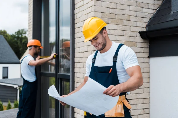 Selektiver Fokus fröhlicher Bauarbeiter auf Baupläne in der Nähe von Mitarbeitern — Stockfoto