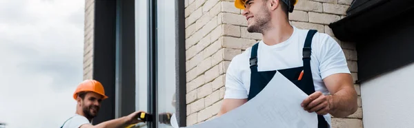 Panoramic shot of happy architect holding blueprint near coworker — Stock Photo