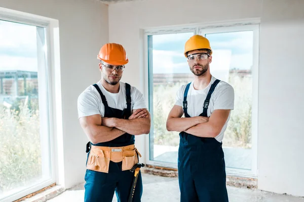 Handsome handymen in helmets and goggles standing with crossed arms — Stock Photo
