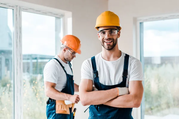 Happy repairman in goggles standing with crossed arms near coworker — Stock Photo
