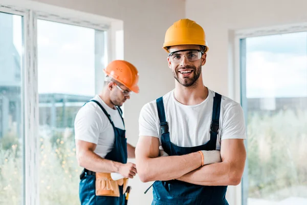 Reparador feliz en gafas de pie con brazos cruzados cerca de compañero de trabajo - foto de stock