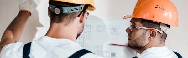 Panoramic shot of architects in helmets looking at blueprint — Stock Photo