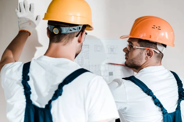 Selective focus of architect in helmet looking at blueprint near coworker — Stock Photo