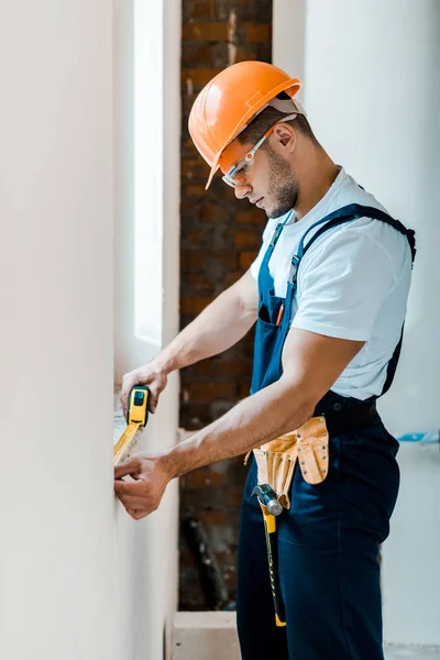 Handsome handyman measuring wall with yellow measuring tape — Stock Photo