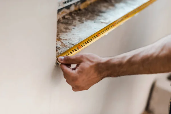 Vista recortada de la pared de medición reparador con cinta métrica amarilla - foto de stock