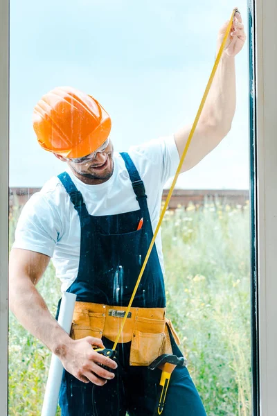 Selective focus of happy repairman measuring window with yellow measuring tape — Stock Photo